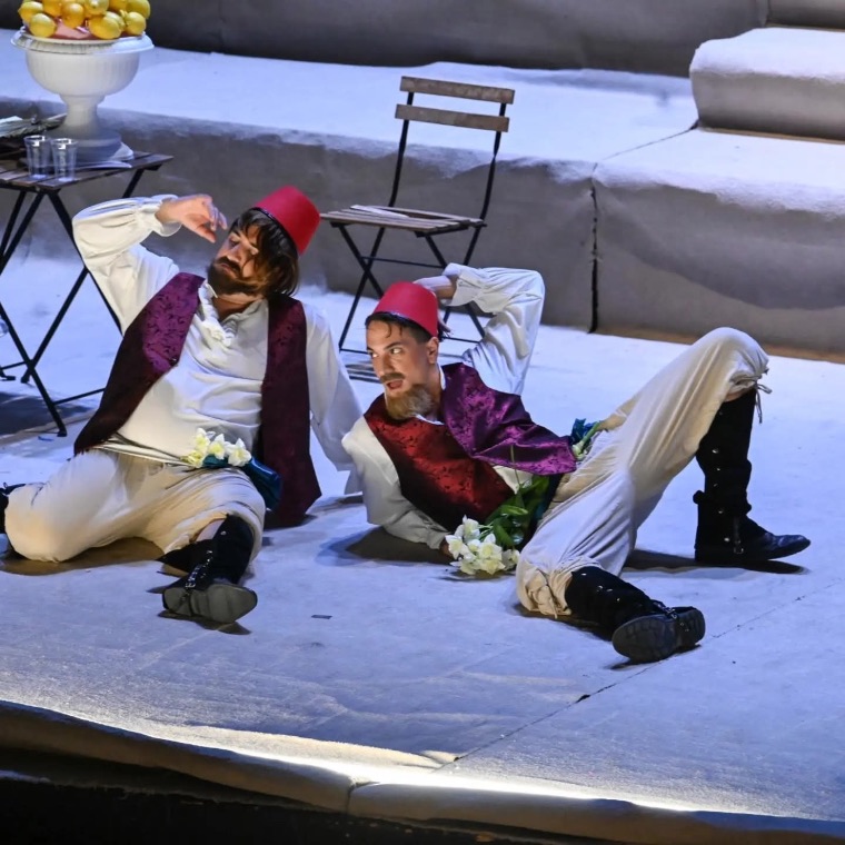 Two characters in fezzes reclining on stage
