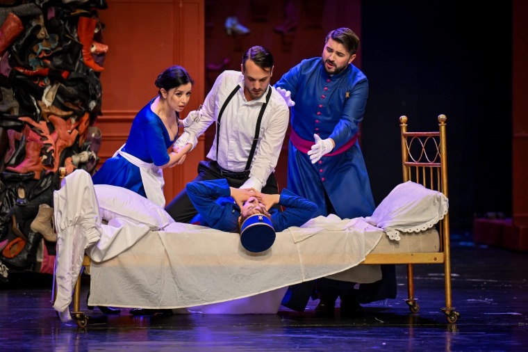 Luka Jozic in an ensemble scene around a brass bed